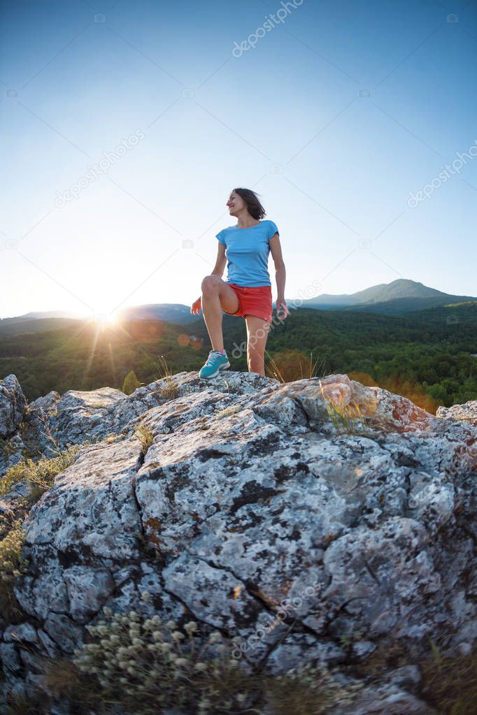 A girl is running in the mountains. A woman goes in for sports in nature. Slender brunette on top of a mountain at sunset.