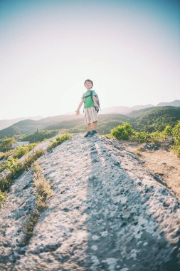 Gün batımında dağın zirvesine çocuğa. Bir çocuk bir sırt çantası ile ilginç yerlere seyahat. Çocuk dağ yolunda yürüyor. Aktif tatiller. Küçük bir seyahat. Tırmanma.