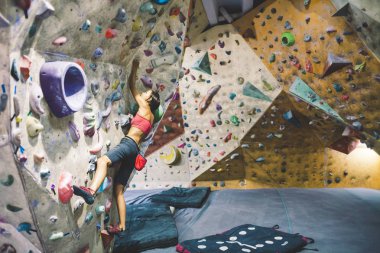 Tırmanma duvarı dağcı trenlerde. Bir kadın üzerinde yapay bir rahatlama tırmanmak eğitiyor. Spor için bir ince kız gider.