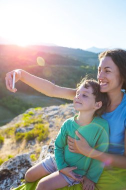 Bir kadın bir dağın tepesinde bir çocukla. Anne ve oğlu selfie güzel bir manzara arka plan üzerinde olun. Bir çocukla seyahat.