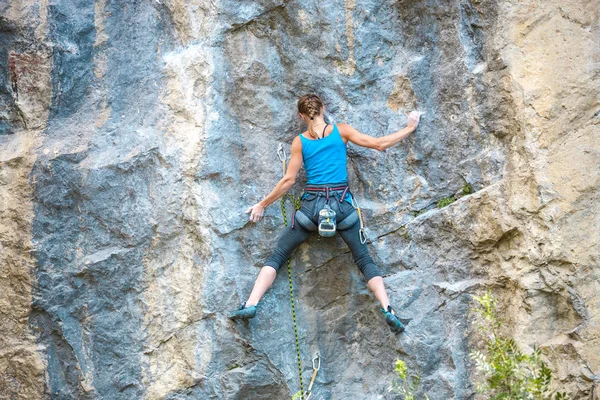 The girl climbs the rock. The climber is training to climb the rock. A strong athlete overcomes a difficult climbing route. Extreme hobby. A woman goes in for sports in nature. Natural rocky terrain.