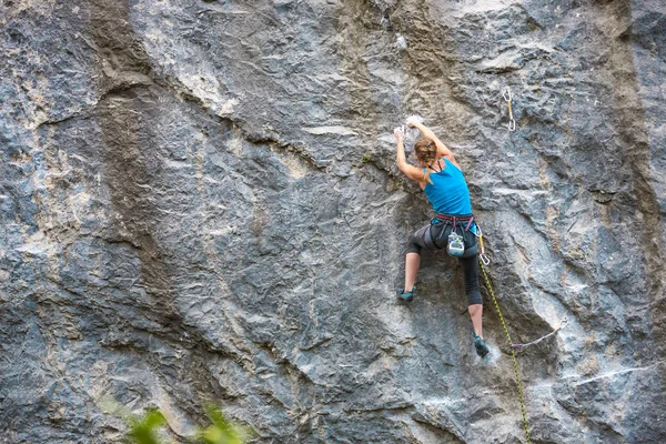 The girl climbs the rock. The climber is training to climb the rock. A strong athlete overcomes a difficult climbing route. Extreme hobby. A woman goes in for sports in nature. Natural rocky terrain.