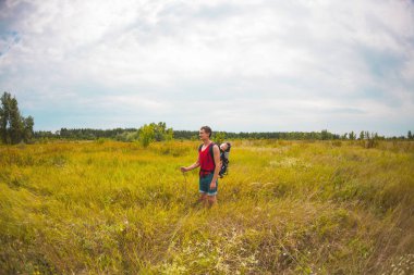 Bir adam bir çocuk bir sırt çantası içinde taşır. Çocuklarla seyahat. Çocuğun babası alanı boyunca ile yürür. Aktif yaşam tarzı.