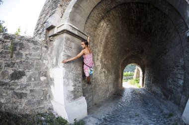 Bir kadın elbiseli bir tuğla duvara tırmanıyor. Kız taş bir çite tırmanıyor. Tırmanıcı bir şehir sokak üzerinde. Eski yıkılan binanın duvarına. Balık gözü lens.