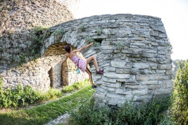 Kız taş duvara tırmanıyor. Bir yaz içinde bir kadın bir eski yıkılan bina duvara tırmanıyor. Tuğla çit. Dağcı şehir bina üzerinde asılı duruyor. Yıkık kalede güçlendirilmesi.