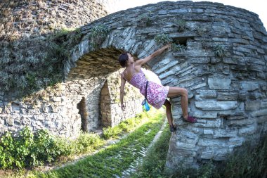 Bir kadın elbiseli bir tuğla duvara tırmanıyor. Kız taş bir çite tırmanıyor. Tırmanıcı bir şehir sokak üzerinde. Eski yıkılan binanın duvarına.