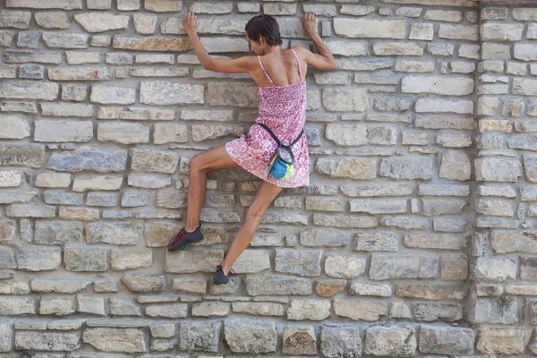 The girl climbs the stone wall. A woman in a summer dress climbs the wall of an old destroyed building. Brick fence. The climber is hanging on the city building. Strengthening the ruined castle.