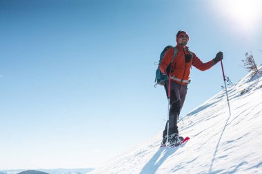 Bir adam dağın zirvesine tırmanıyor. Dağcı kar ayakkabıları bir sırt çantası taşımak. Yolculuk kışın dağlarda. Doğada aşırı tatil. Aşırı koşullarda Turizm.