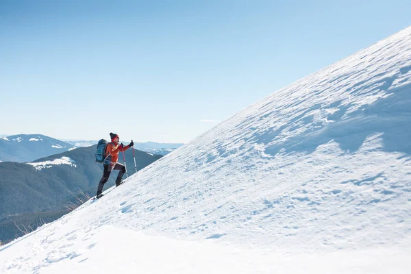 A man climbs to the top of the mountain. Mountaineer in snow shoes carry a backpack. Journey in the mountains in winter. Extreme vacation in nature. Tourist in extreme conditions.