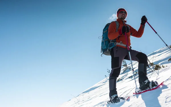 A man climbs to the top of the mountain. Mountaineer in snow shoes carry a backpack. Journey in the mountains in winter. Extreme vacation in nature. Tourist in extreme conditions.
