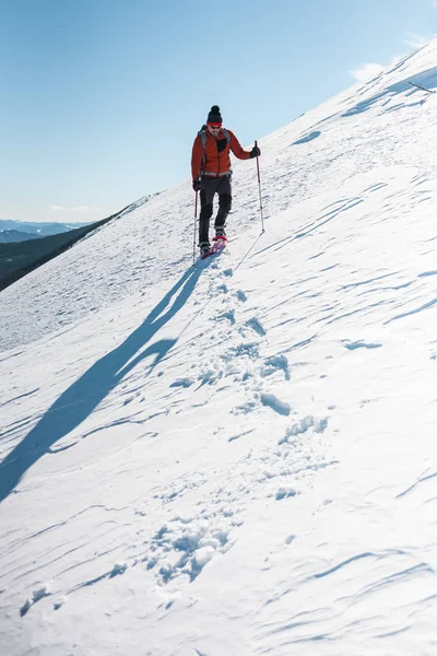 Bir adam dağın zirvesine tırmanıyor. Dağcı kar ayakkabıları bir sırt çantası taşımak. Yolculuk kışın dağlarda. Doğada aşırı tatil. Aşırı koşullarda Turizm.