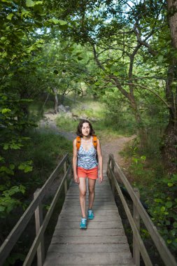 Bir sırt çantası bir kızla bir ahşap köprü yürür. Kadın dolaşıyor. Ormanda yürümek. Nehir ince bir esmer haçlar.