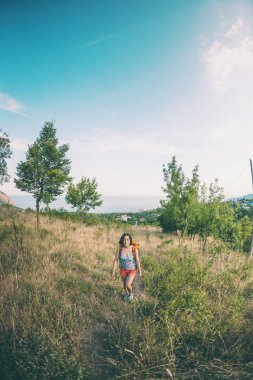 Bir kadın bir sırt çantası ile dolaşıyor. Kız dağın tepesine tırmandı. Esmer dağ yolunda yürüyor.