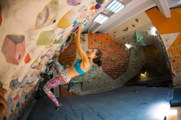 Strength and endurance training. The climber trains on the climbing wall. A woman trains to climb on an artificial relief. A slender girl goes in for sports. Fisheye lens.