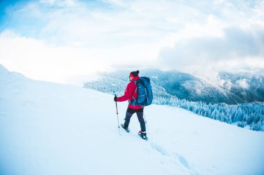 Kar ayakkabılarını ve dağlarda trekking sopalarla bir adam. Kış gezi. Güzel bir gökyüzü bulutlu karşı bir dağcı, tırmanma. Aktif yaşam tarzı. Karda dağ tırmanma.