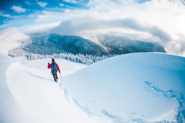 Kışın dağlarda kar ayakkabıları bir adam. Bir dağcı trekking sopa ile kar üzerinden yürür. Kış tırmanışı. Güzel gökyüzü bulutlu.