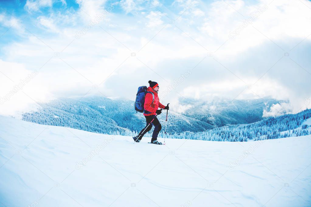 A man in snowshoes and trekking sticks in the mountains. Winter trip. Climbing of a climber against a beautiful sky with clouds. Active lifestyle. Climbing the mountain through the snow.