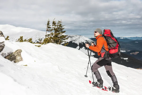 Winter climbing the mountain. A man in snowshoes is climbing to the top. Winter ascent. A mountaineer with a backpack and trekking sticks. Equipment for winter hiking.