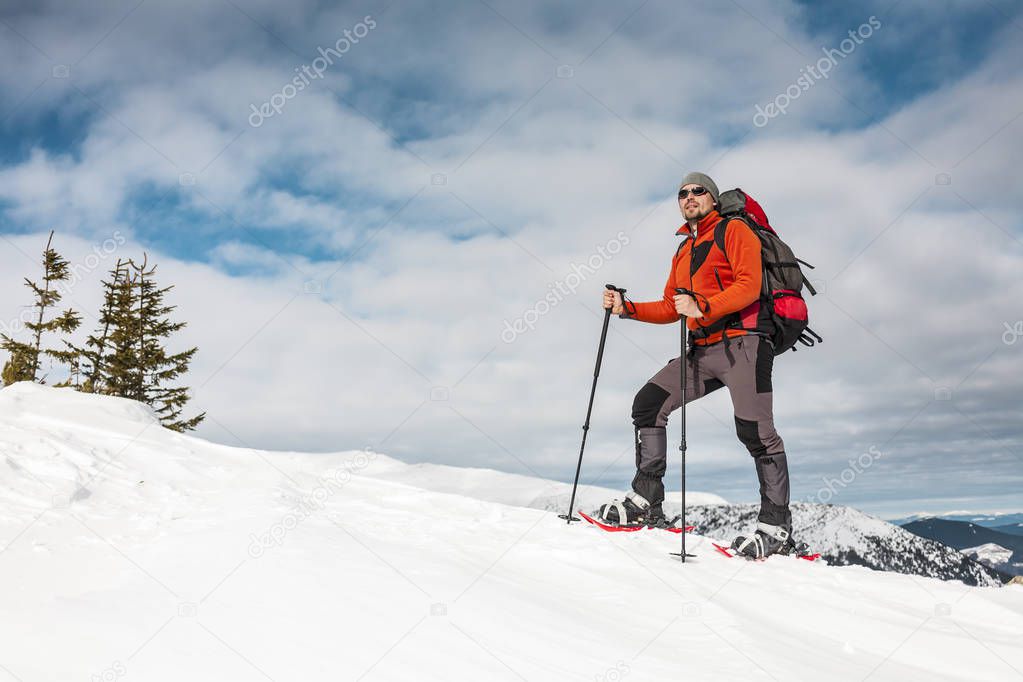 Winter climbing the mountain. A man in snowshoes is climbing to the top. Winter ascent. A mountaineer with a backpack and trekking sticks. Equipment for winter hiking.