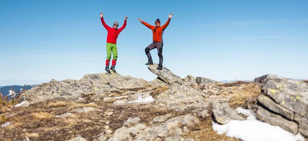 Two mountaineers climbed to the top of the mountain. Men are balancing on the rocks. Friends in the mountain hiking. The climbers raised their hands up.