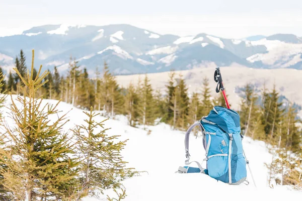 Backpack on the background of snow-capped mountains and blue sky. A backpack on the snow. Active lifestyle. Trekking in winter. Equipment for hiking. Trekking sticks.