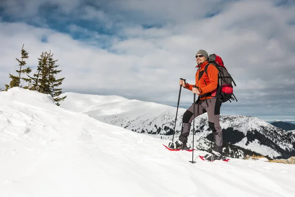 A man climbs to the top of the mountain. Mountaineer in snow shoes carry a backpack. Journey in the mountains in winter. Extreme vacation in nature. Tourist in extreme conditions.