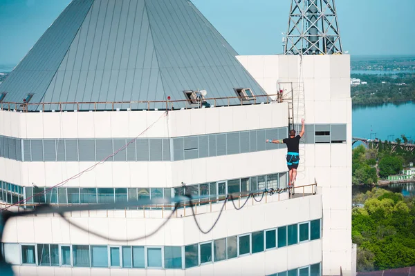 A man walks along a line stretched between two buildings. Extreme entertainment. Fear of heights. The man is balancing over the city.