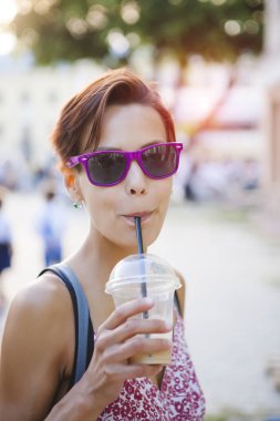 Bir kadın sokakta onun susuzluk quenches. Bir kız bir şehir sokak bir kokteyl içer. Kahve. Esmer bir tüp ile süt içecek içecekler.