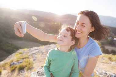 Bir kadın bir dağın tepesinde bir çocukla. Anne ve oğlu selfie güzel bir manzara arka plan üzerinde olun. Bir çocukla seyahat.