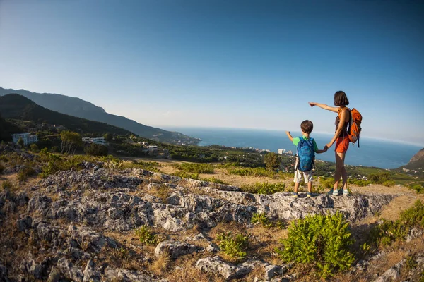 A woman is traveling with a child. Mom and son in the mountains. Climb to the top of the mountain with children. The kid with the backpack climbed to the top. The boy raised his hands up.