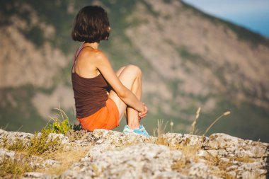 Bir kız günbatımında bir dağın tepesinde oturuyor. Bir kadın yoga yapan ve lotus pozisyonda oturuyor. Meditasyon medeniyet çok uzak olduğunu. Güzel kadın geri. Dağlar ve deniz görünümü.