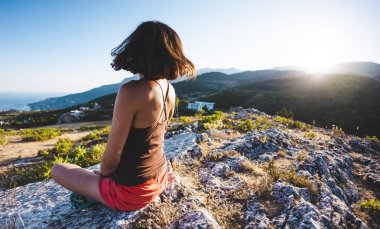 Bir kız günbatımında bir dağın tepesinde oturuyor. Bir kadın yoga yapan ve lotus pozisyonda oturuyor. Meditasyon medeniyet çok uzak olduğunu. Güzel kadın geri. Dağlar ve deniz görünümü.