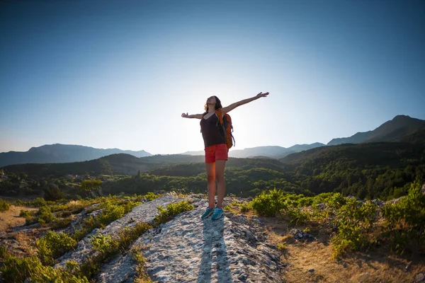 女孩在山顶上 一个背着背包的女人站在石头上举起手 爬上山顶 旅行到风景如画的地方 游客对天空 — 图库照片