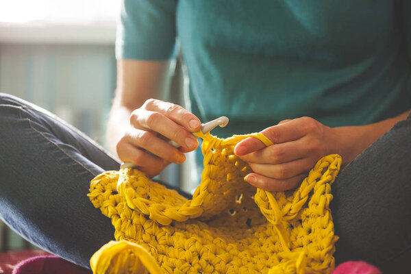 Woman knits crochet. The girl sits on the couch and knits from knitting yarn. Crochet thick threads. Home comfort.