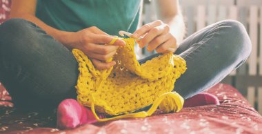 Woman knits crochet. The girl sits on the couch and knits from knitting yarn. Crochet thick threads. Home comfort. clipart