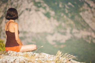 Bir kız günbatımında bir dağın tepesinde oturuyor. Bir kadın yoga devreye girer. Meditasyon medeniyet çok uzak olduğunu. Güzel doğa ve tefekkür. Dağları nın görünümü. Güzel gün batımı ışık.