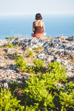 Bir kız günbatımında bir dağın tepesinde oturuyor. Bir kadın yoga yapan ve lotus pozisyonda oturuyor. Meditasyon medeniyet çok uzak olduğunu. Güzel kadın geri. Dağlar ve deniz görünümü.
