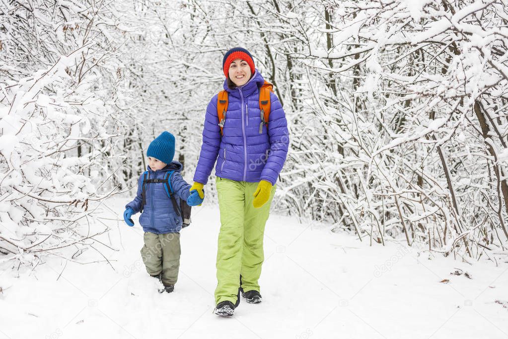 The boy walks with his mother on a snow covered forest path. Winter holidays. A child with a backpack is having fun with his mother.