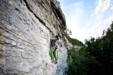 Bir kadın zor bir tırmanış rota üstesinden gelir. Spor kız kayaya tırmanıyor. Güç ve dayanıklılık eğitim. Atlet üzerinde doğal bir rahatlama tırmanıyor.