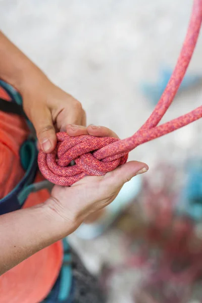 A climber knits a knot. A woman prepares to climb a climbing route. Insurance and safety in rock climbing. Safety rope. Node eight.