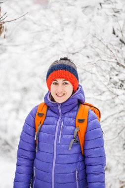 Bir sırt çantası içinde kış olan kadın. Bir kız bir orman yolu yürüyor. Karla kaplı ağaçlar parkta. Uzun bir yürüyüş üzerinde sıcak giysiler içinde gülümseyen kız.