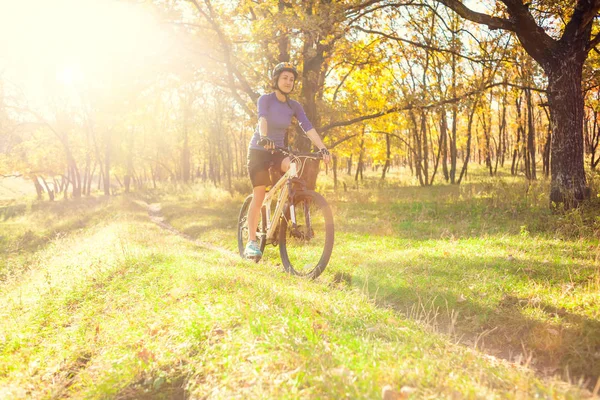 Biking in the forest. Girl rides a bike on a forest trail. Woman riding her bike in the park. Bicycle touring. Travel to scenic places. Autumn trees.