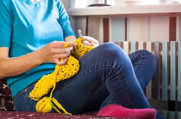 Woman knits crochet. The girl sits on the couch and knits from knitting yarn. Crochet thick threads. Home comfort.