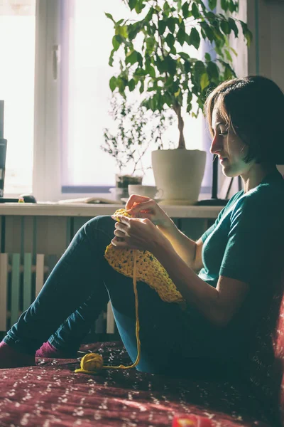 Girl knits crochet at home. Woman engaged in needlework. A knitter sits on a sofa and works. Creative hobby. Training patience and perseverance. Crochet thick yarn.