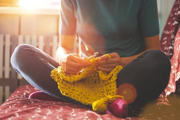 Woman knits crochet. The girl sits on the couch and knits from knitting yarn. Crochet thick threads. Home comfort.