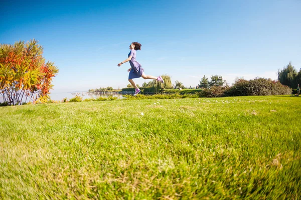 Uma menina em um vestido corre por um prado verde . — Fotografia de Stock