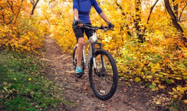 Bir sırt çantası ile kız sonbahar parkta bisiklete biniyor. Doğada ince kadın trenler. Ormanda spor. Turistik bir kir iz sürmek. Bisikletle seyahat.