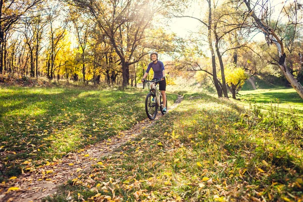 Biking in the forest. Girl rides a bike on a forest trail. Woman riding her bike in the park. Bicycle touring. Travel to scenic places. Autumn trees.