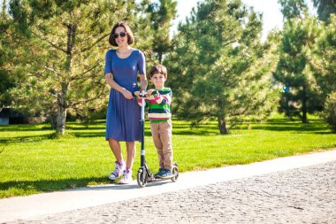 Çocuk annesi ile bir scooter sürmek. Çocuk Parkı üst ile vakit geçiriyor. Bir kadın bir scooter binmek için oğlunu öğretir. Anne ile ortak eğlence.