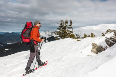 Kış dağ tırmanışı. Kar ayakkabılarını erkeklerde zirveye tırmanıyor. Kış tırmanışı. Bir sırt çantası ve trekking sopa ile bir dağcı. Kış yürüyüş için donatım.